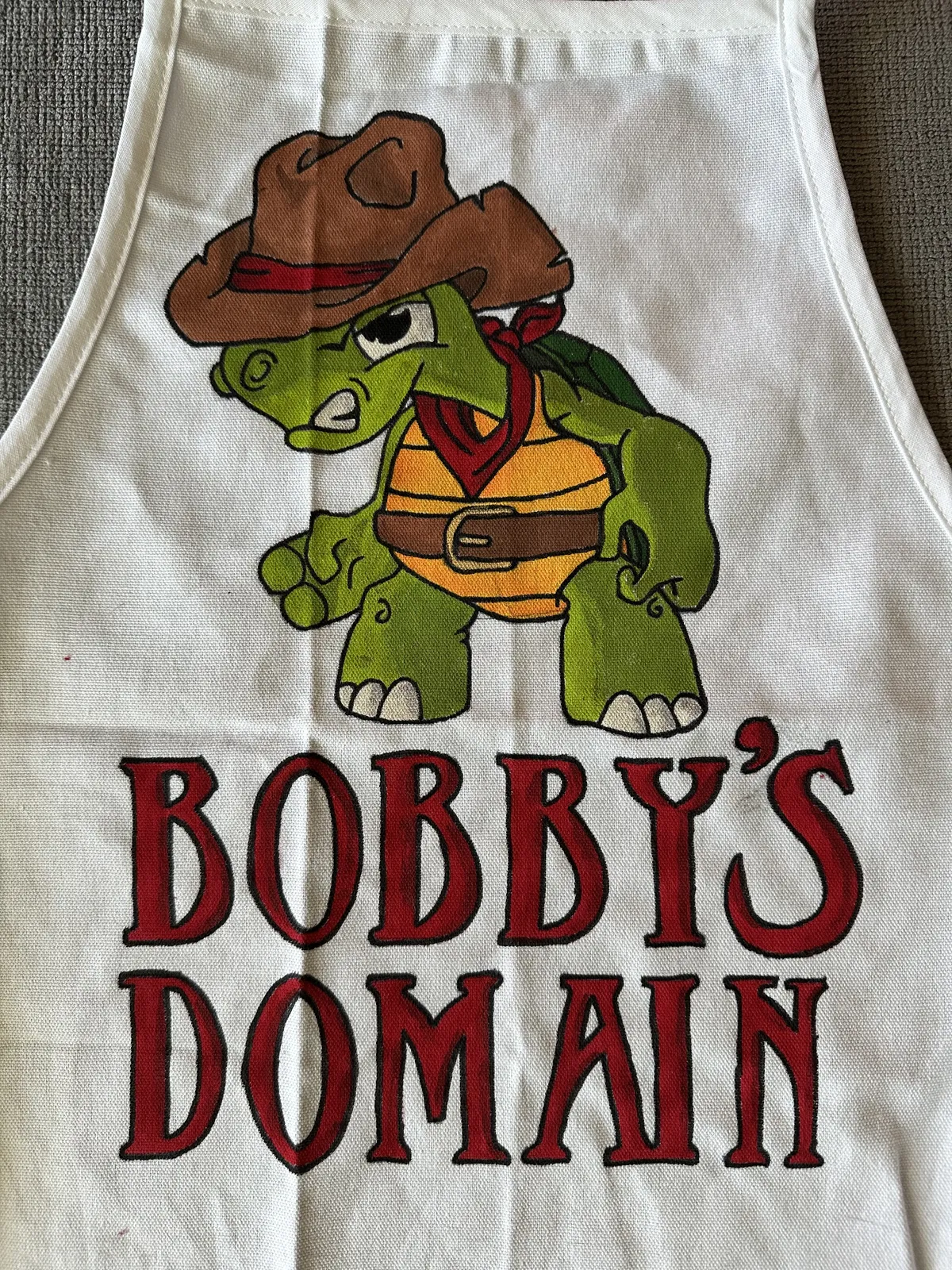 Hand-painted apron with a cowboy turtle and the words Bobby’s Domain