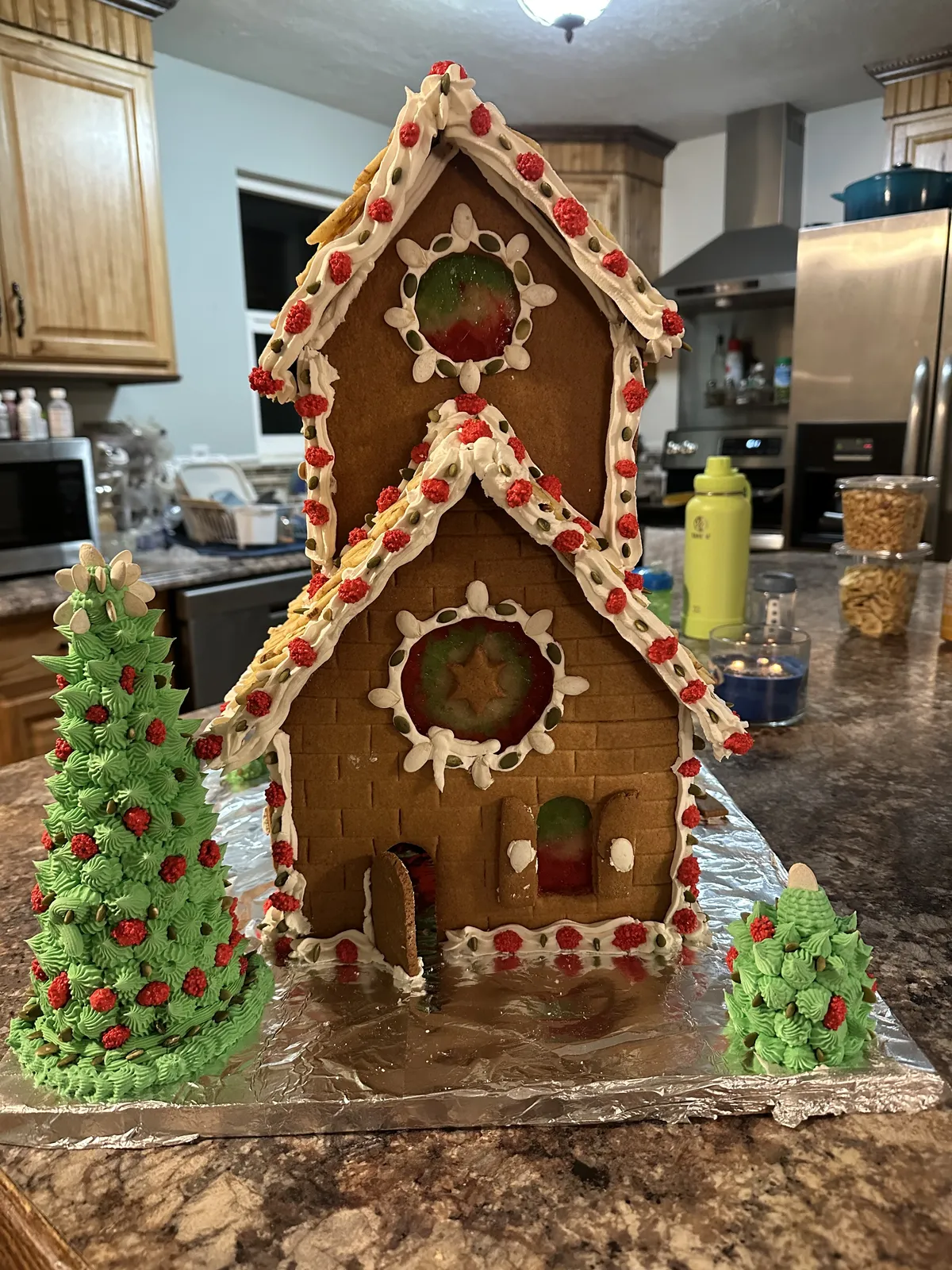 Front of a two-story gingerbread house with candy windows and frosted trees